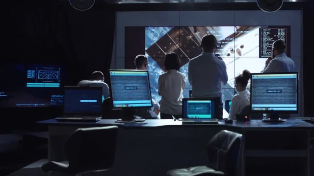Back view of people working and managing flight in mission control center. Elements of this image furnished by NASA.