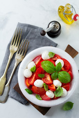 Traditional Italian caprese salad with tomatoes, mozzarella cheese and basil on a light marble background in a white old ceramic plate. Selective focus.Top view. Copy space.