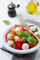 Traditional Italian caprese salad with tomatoes, mozzarella cheese and basil on a light marble background in a white old ceramic plate. Selective focus.Top view. Copy space.