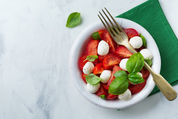 Traditional Italian caprese salad with tomatoes, mozzarella cheese and basil on a light marble background in a white old ceramic plate. Selective focus.Top view. Copy space.