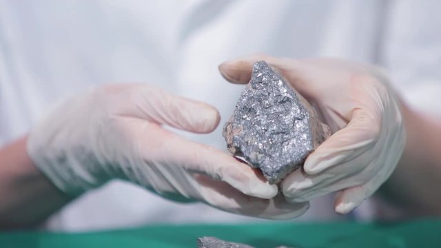 Female hands in white gloves holding stone mineral. Stone macro, gray rough stone. Fluorite mineral stone, fluorite mineral stone. Scientist studying the stone material close up
