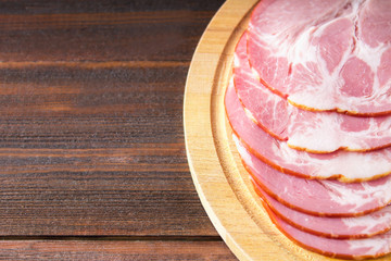 Sliced ham with fresh green lettuce leaves on a round cutting board. Meat products on a brown wooden table.