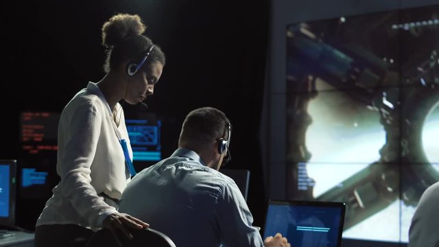 Black and white woman and man monitoring in dark room of space mission control center. Outer works of astronauts. Elements of this image furnished by NASA.