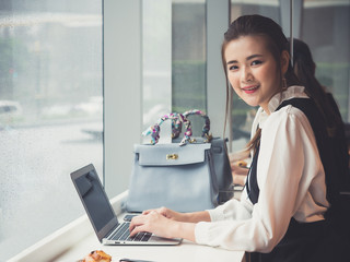 Young asian businesswoman working on laptop at coffee shop cafe during raining, smiling and happy working.