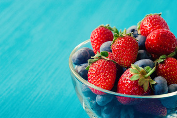 mixed berries in a a transparent cup on brown wooden background