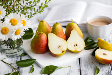 Summer romantic still life. Fresh ripe organic Pears, bouquet of field daisy flowers, cup of coffee, book. High key style photo. White table surface for background. Natural healthy lunch.