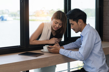 Smiling young couple in a coffee shop using touch screen smartphone. Young man and woman in a restaurant looking at smartphone. Technology and Lifestyle Concept