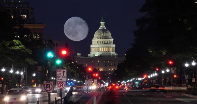 A night time lapse view of traffic activity on Pennsylvania Avenue in Washington, D.C. with the Capitol Dome in the distance. A nearly full moon in the sky.  	