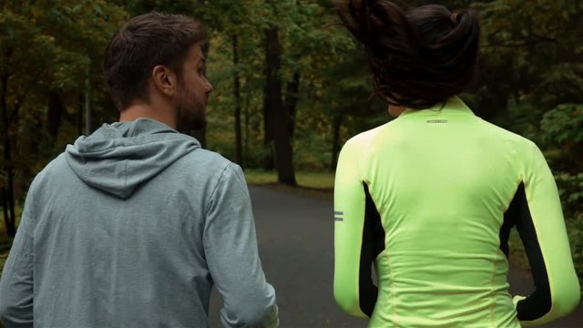 Tracking slow-motion of girl and guy communicating and smiling during morning jog. They running at the park and has a conversation on asphalt road. Rapidly slomo phantom flex back shot