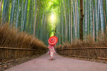 Schilderijen op glas Vrouw in traditionele Yukata met rode paraplu bij bamboebos van Arashiyama © f11photo