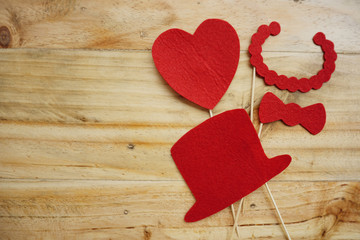 Top or flat lay view of Photo booth props a red heart shape, a red hat and a red necklace on a wooden background flat lay. Birthday parties and weddings.