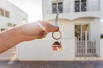 Holding house keys on house shaped keychain closeup in front of a new home. Concept of real estate
