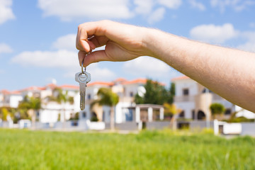 Holding house keys on house shaped keychain closeup in front of a new home. Concept of real estate