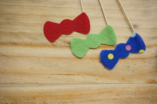 Top or flat lay view of Photo booth props a red bow tie, green bow tie and a blue polkadot bow tie on a wooden background flat lay. Birthday parties and weddings.