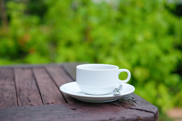 white coffee cup on wooden table in the garden, coffee break in the morning with sunlight.