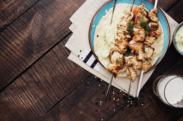 Barbecued chicken breast skewers on wooden table with border