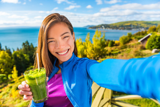 Healthy green smoothie juice drinking selfie girl taking picture clean food diet healthy nutrition. Asian woman eating fresh spinach vegetable juicing in beautiful outdoors autumn nature.