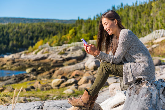 Happy Girl Texting Sms Message On Mobile Phone On Nature Forest Hike In Autumn Outdoors. Asian Woman Playing On Cellphone