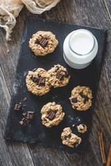 Obraz na płótnie Canvas Homemade oatmeal raisin cookies with chocolate and milk on slate background. Selective focus, toned image