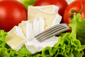 Tomatoes and cheese slices lie on a sheet of fresh salad in a red plate.