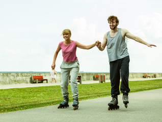 Fototapeta premium Young couple rollerblading in park holding hands.