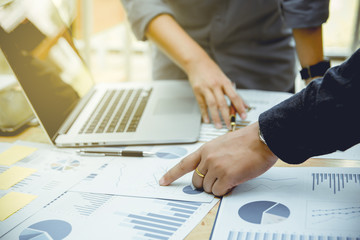 Hand of businessman pointing graph paper on wooden table in office.