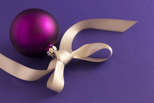 Beautiful purple christmas ball with satin effect and grey gift ribbon on purple background.