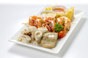 Mixed Roasted Seafood (Small Platter Set) Contain Grilled Big Shrimps, Calamari Squids and Barracuda Fish Garlic Pepper with Spicy Chili Sauce and Potatoes, High Angle View, Selective Focus at Food.