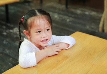 Happy cute little girl lying on the wood table looking out. Back to School concept.