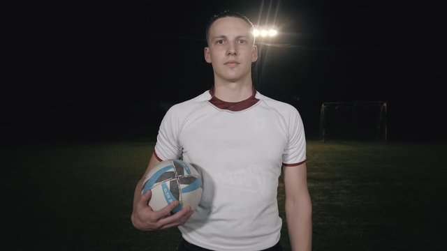 Rugby fan player in arena against rugby players training with ball, dark football arena, close up portrait