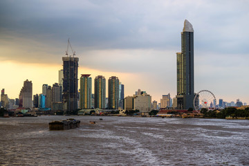 Bangkok skyline cityscape. Buildings, river and boat transportation, ferris wheel at twilight with rain storm and dark cloud and  red sky