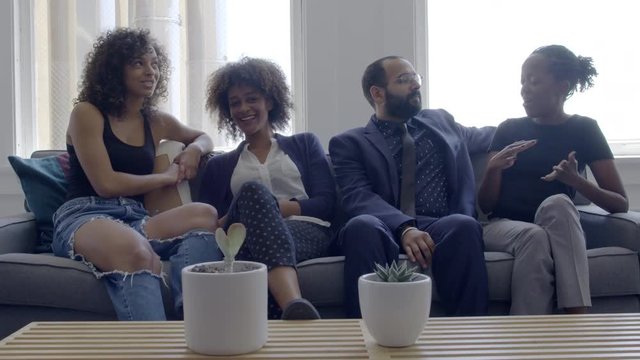 Mixed race group of friends chatting and hanging out on a sofa in a bright, day interior, urban loft or apartment. Slow motion hand-held 4K, recorded at 60fps.