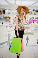 Portrait of a woman in leopard blouse, black skirt walking in shopping mall with bags and talking on the phone.