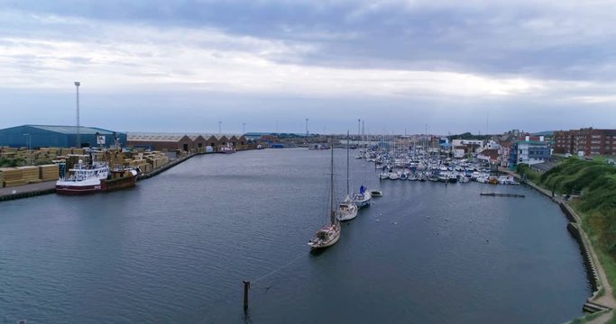 Aerial ascending view of sailing boats in a commercial harbor on a river mouth in Southern England