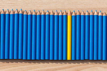Fototapeta premium Des petits crayons de couleur bleu alignés avec un crayon jaune au milieu