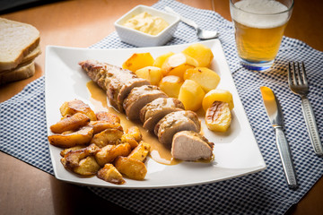 Carn di maiale arrosto con patate e spicchi di mela arrostite servite su un piatto