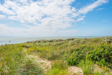 Sand dunes along a coast below a blue cloudy sky in summer