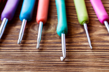 A set of multicolored crochet hooks on a wooden background. Close-up, selective focus