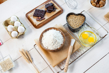 Baking ingredients in rural kitchen - dough recipe ingredients (eggs, flour, milk, butter, sugar) and rolling pin on wooden white table. Top View