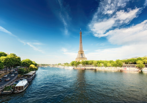 The Eiffel Tower in Paris, France, on a sunny day with the river Seine and dramatic clouds.  Colourful travel background. Popular travel destination