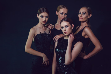 Beautiful women in black cocktail dresses on a dark background.