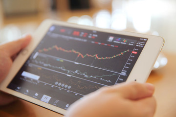 Business Hand Analyzing Stock finance Graph on Tablet with Coffee on wood background