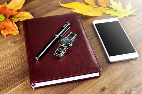 Notepad, pen, clock and phone on a wooden table