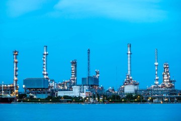 Obraz premium Oil refinery plant near river at twilight, Business and Industry concept