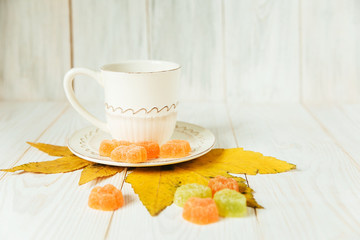 Cup with autumn elements on the white wood.Jelly candy,leaves.Autumn composition.