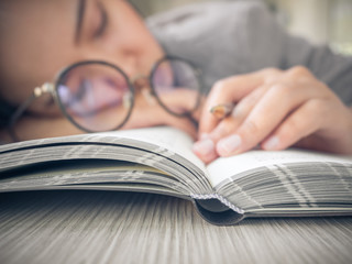 Sleepy student/businesswoman fall asleep on a book with glasses during studying