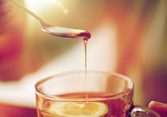 close up of woman adding honey to tea with lemon