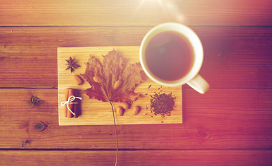 Obraz na płótnie Canvas cup of tea, maple leaf and almond on wooden board