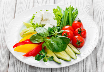 Fresh vegetables plate with feta cheese, cherry tomatoes, cucumber, celery, sweet pepper and basil in a plate on wooden background close up. Top view
