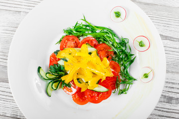 Fresh salad with cherry tomatoes, cucumber, radish, sweet pepper and onion in a plate on wooden background close up. Top view